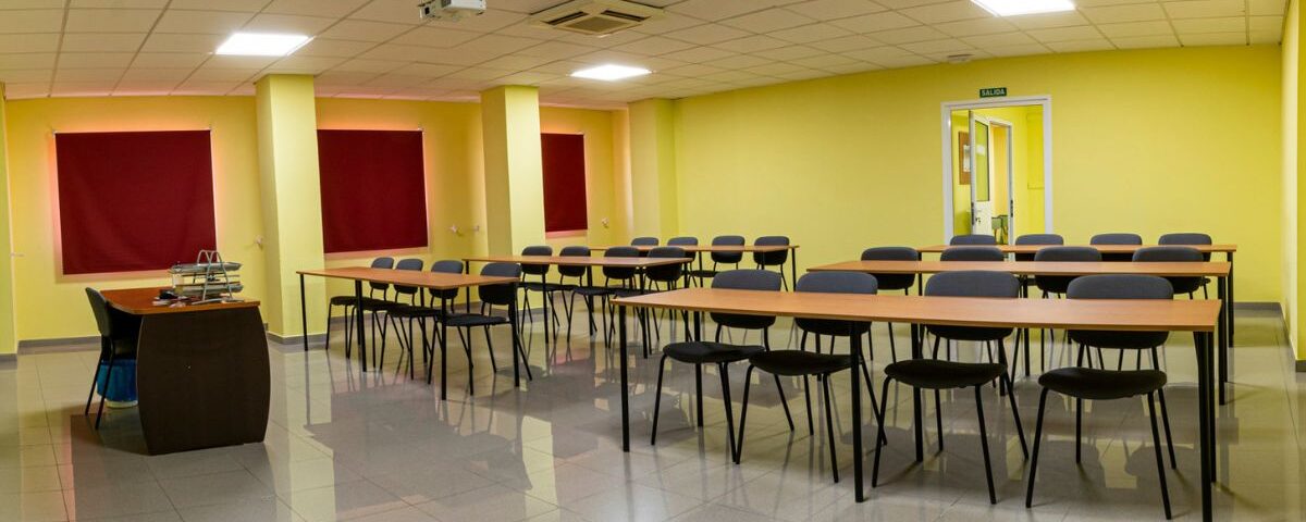 Aula teórica de Autoescuelas Tamarán equipada con mesas, sillas y proyector para clases presenciales.