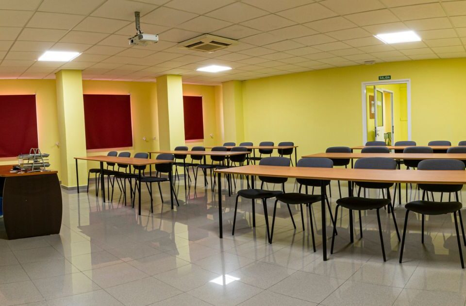 Aula teórica de Autoescuelas Tamarán equipada con mesas, sillas y proyector para clases presenciales.